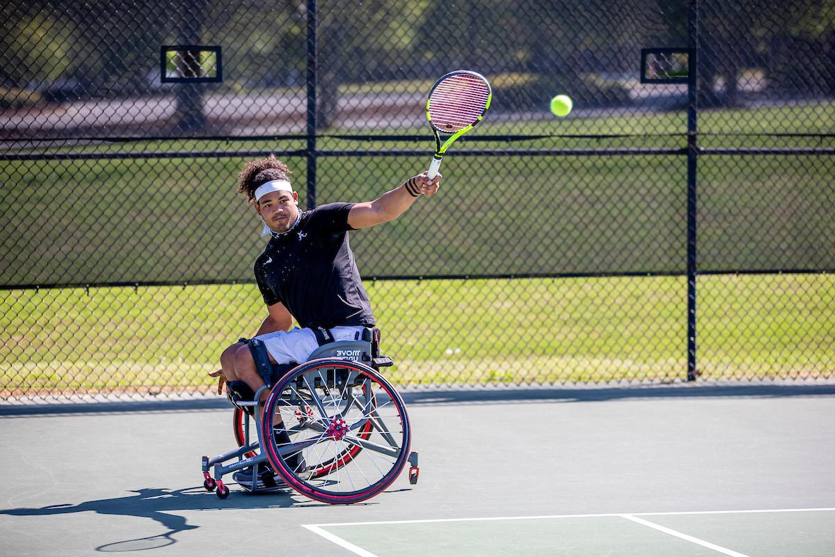 A wheelchair tennis player hits a backhand shot.